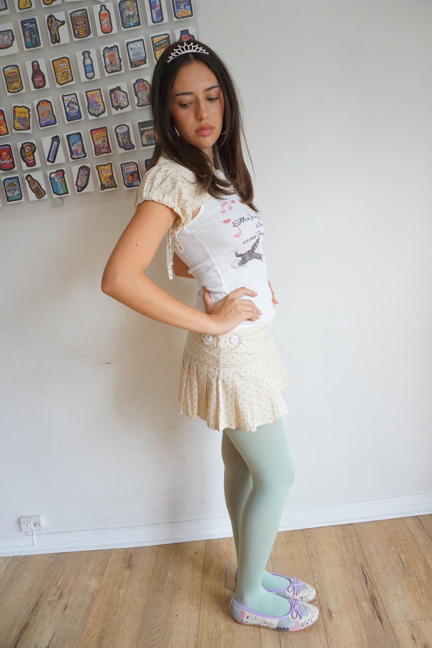 Girl wearing a cream pleated skirt with blue polka dots and a tiara and blue tights