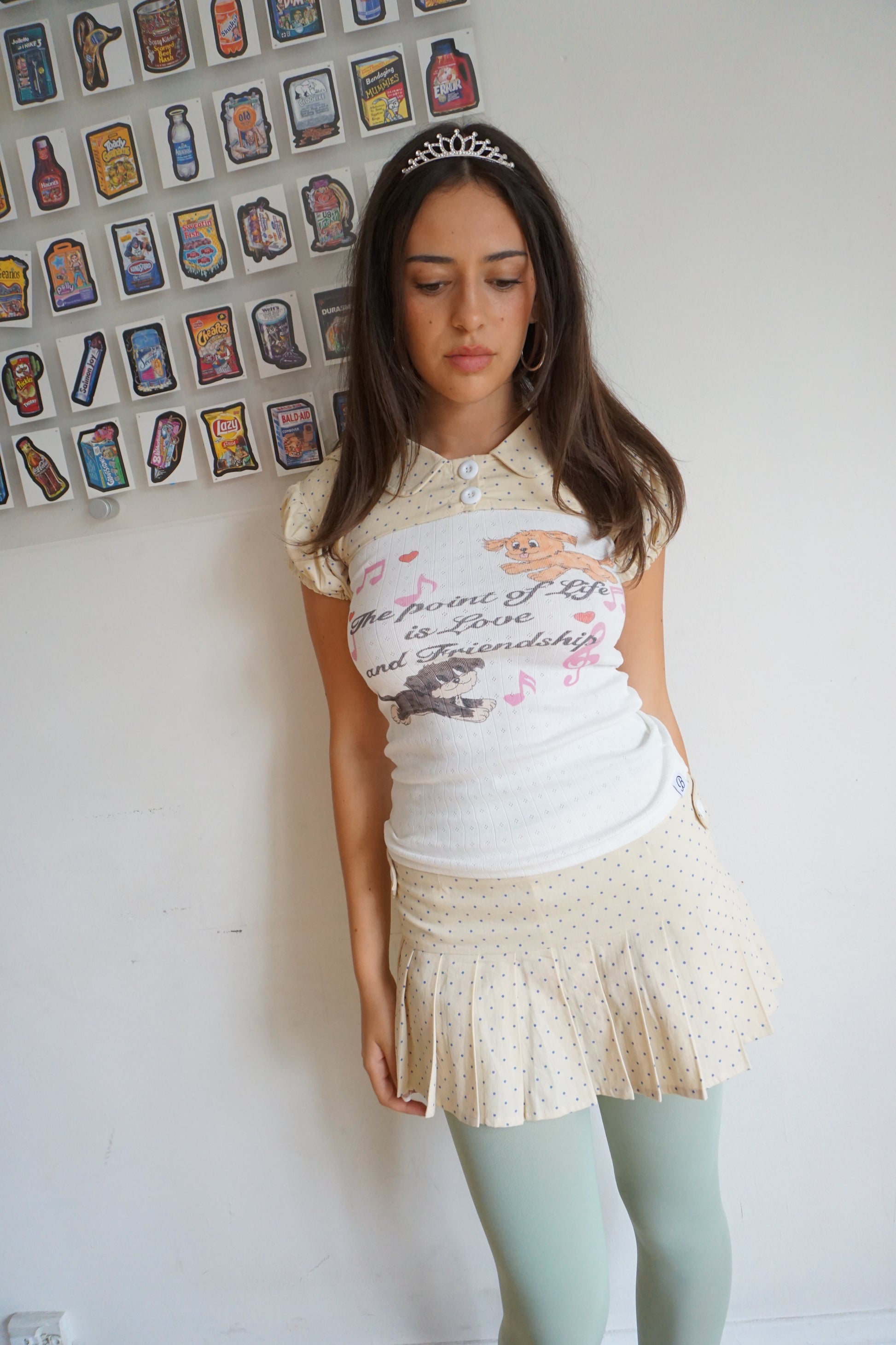 Girl wearing a cream pleated skirt with blue polka dots and blue graphic t shirt
