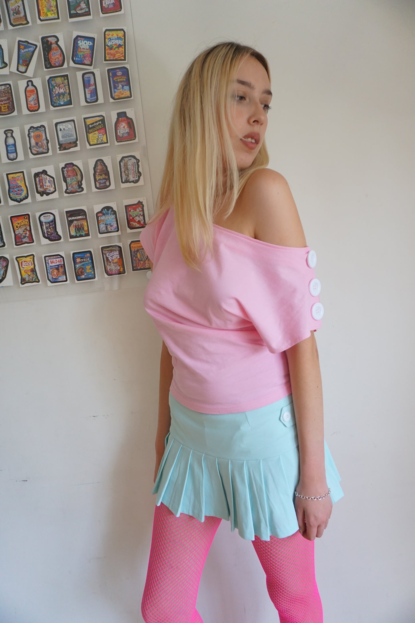 girl wearing. a pink off the shoulder top with buttons on the sleeves and a mint green skirt