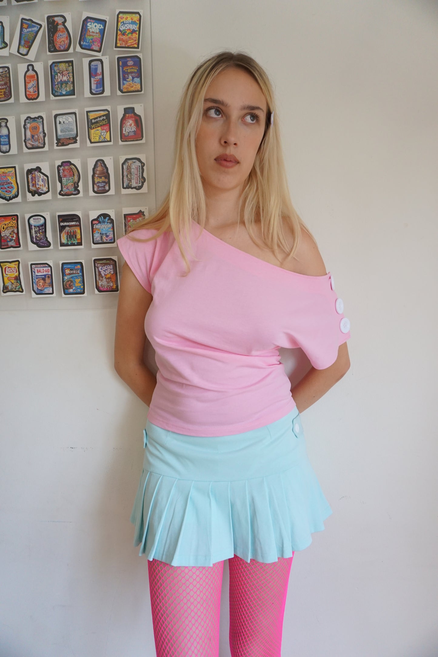 girl wearing. a pink off the shoulder top with buttons on the sleeves and a mint green skirt
