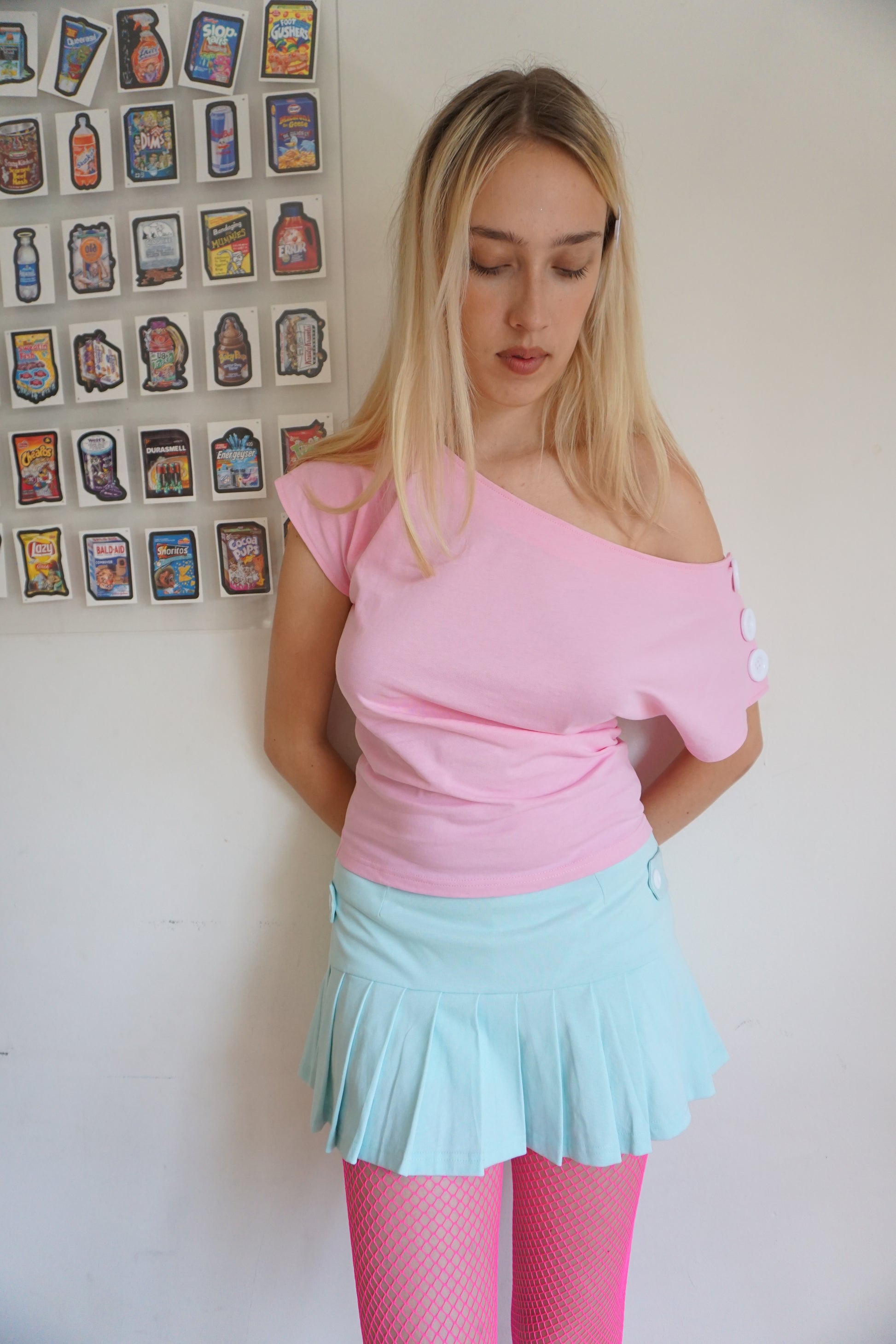 girl wearing. a pink off the shoulder top with buttons on the sleeves and a mint green skirt