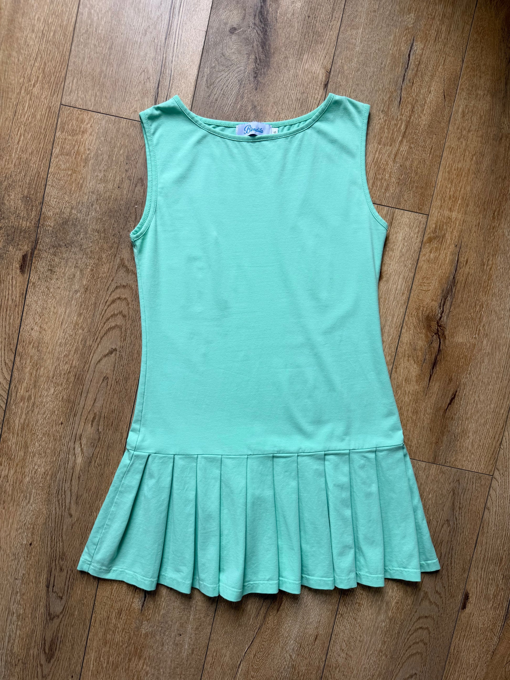 girl wearing a mint green drop waist pleated dress on wood floor