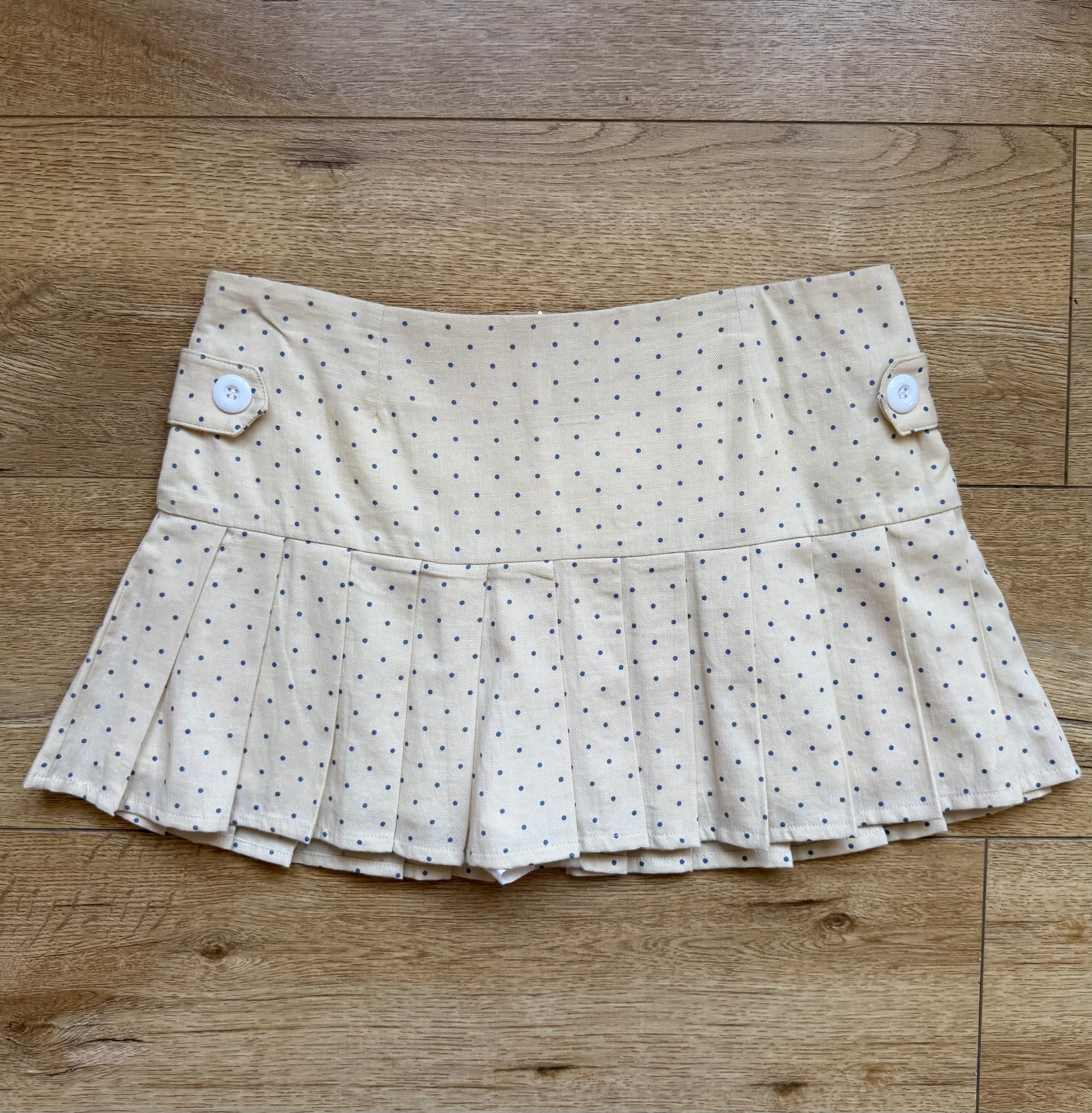Girl wearing a cream pleated skirt with blue polka dots and blue graphic t shirt