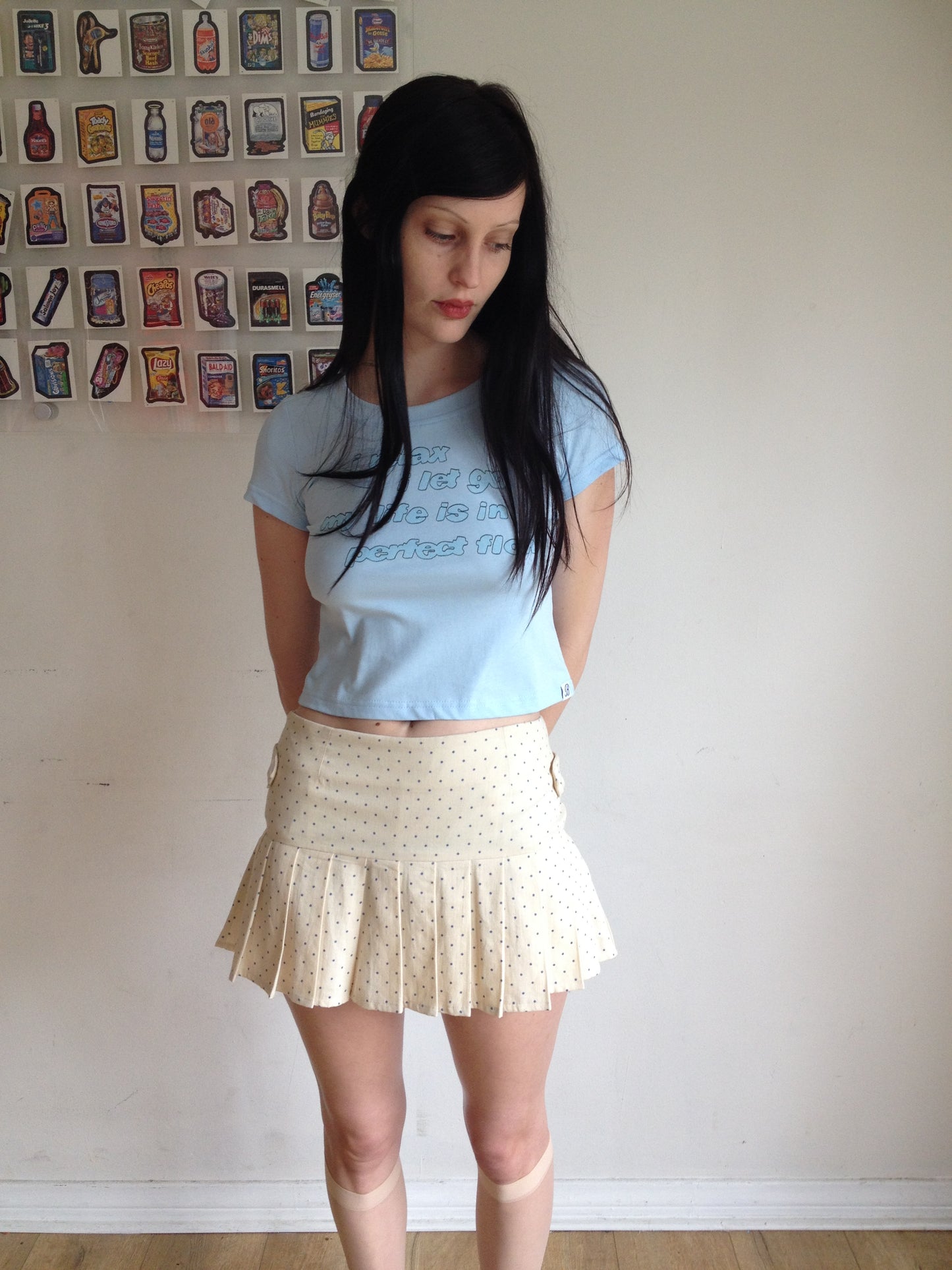 Girl wearing a cream pleated skirt with blue polka dots and blue graphic t shirt