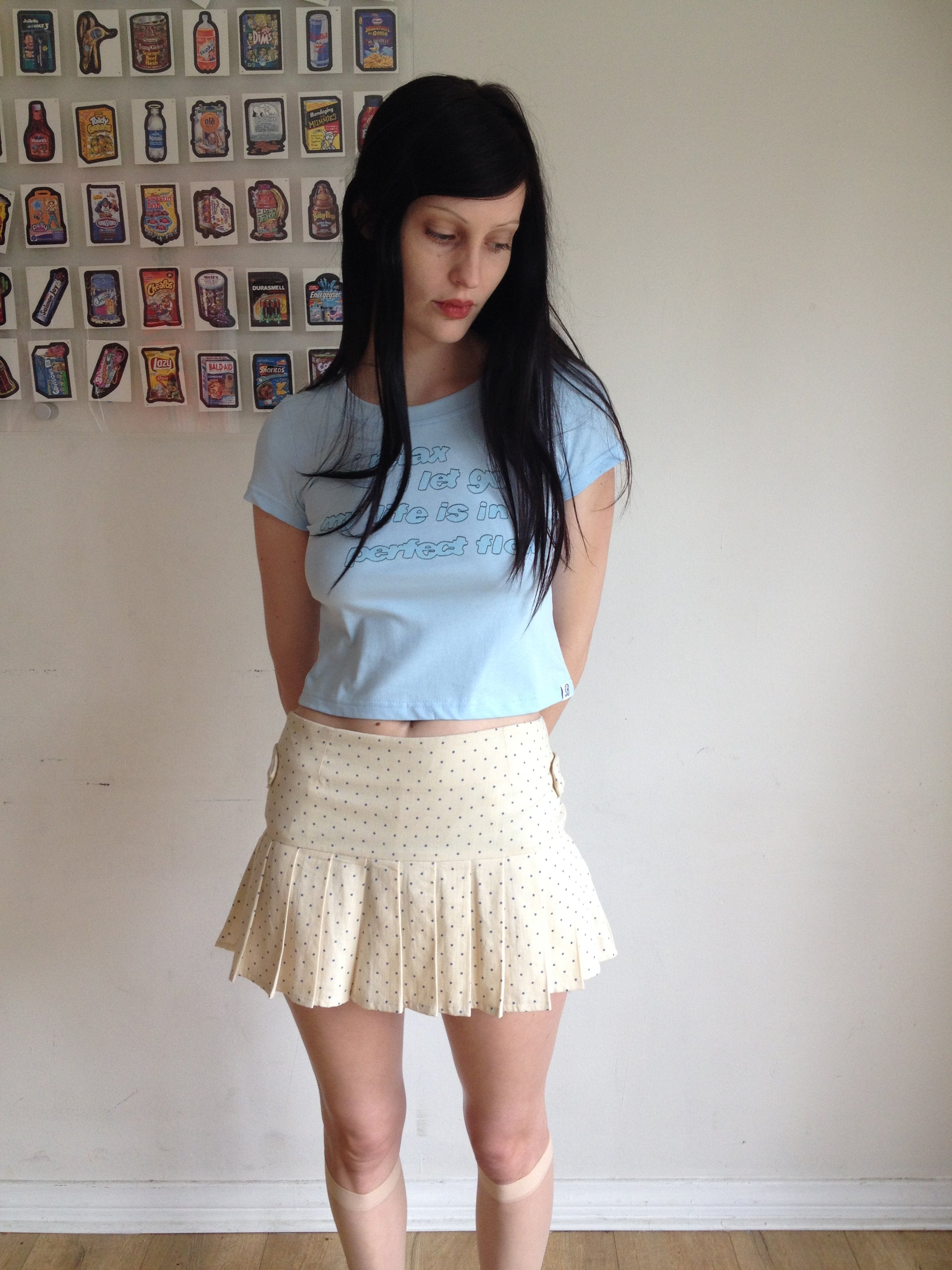 Girl wearing a cream pleated skirt with blue polka dots and blue graphic t shirt