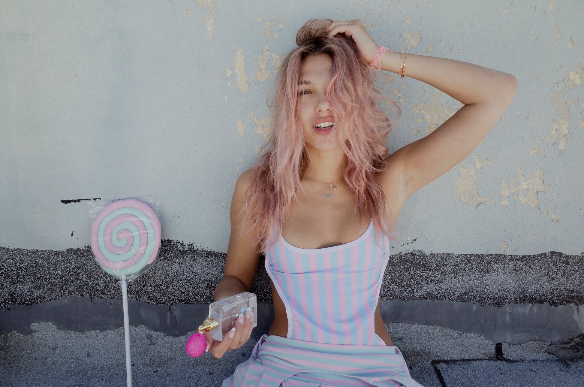 Girl wearing a pink and blue stripe one piece swimsuit with cutouts on side with lollipop
